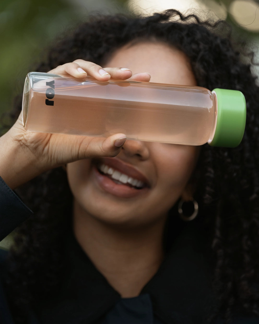 Girl holdin up a YOJ bottle and smiling. Tags for product images: grüner, blauer, gelber, rosa, schwarzer